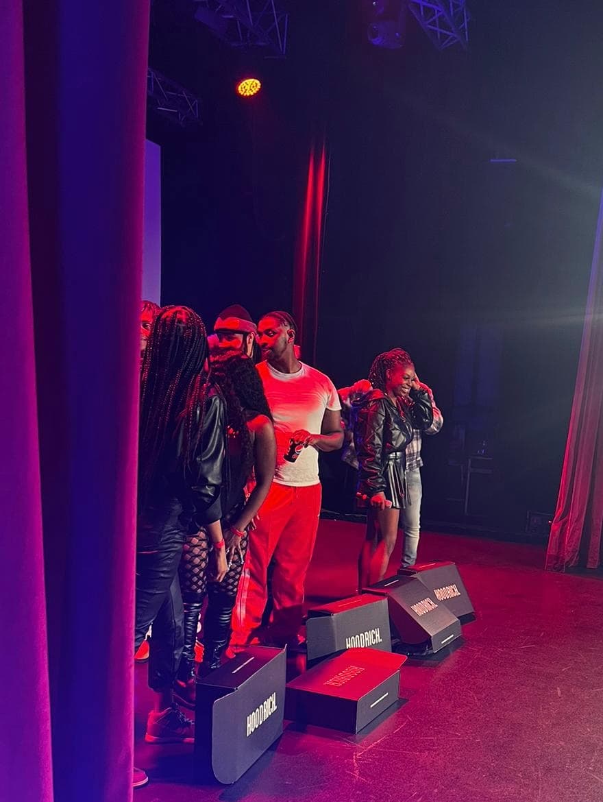 People stand on a stage with red lighting, purple curtains, and Hoodrich branded monitors.